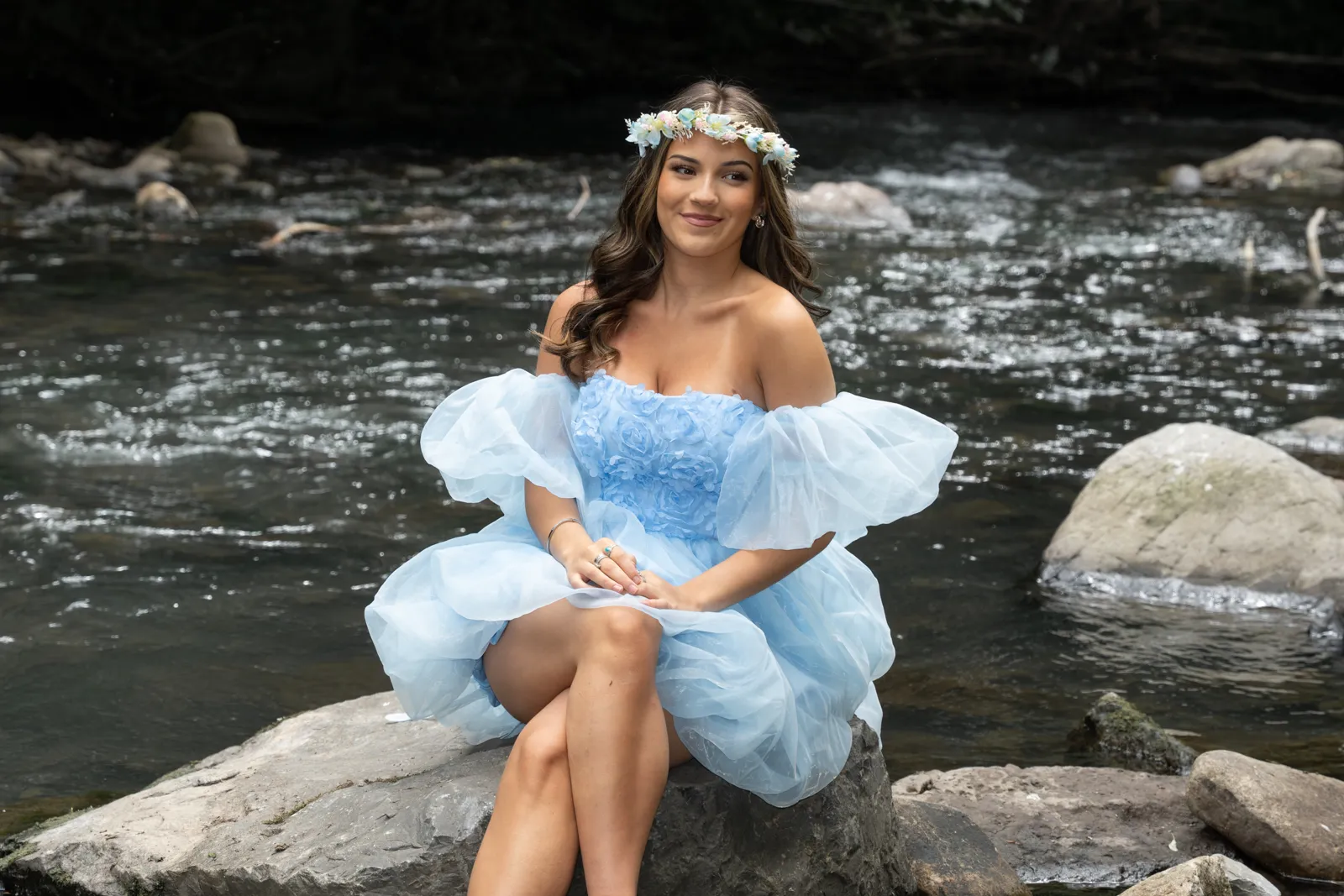 girl dressed in a blue dress by a river, sitting on a rock